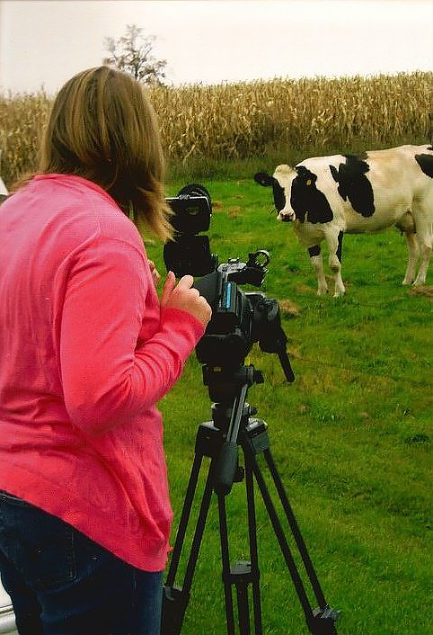 Holly De Ruyter is seen from the back as she films a black and white cow in a field