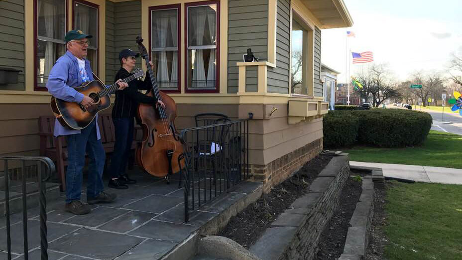 Man playing guitar and woman playing upright base on front porch