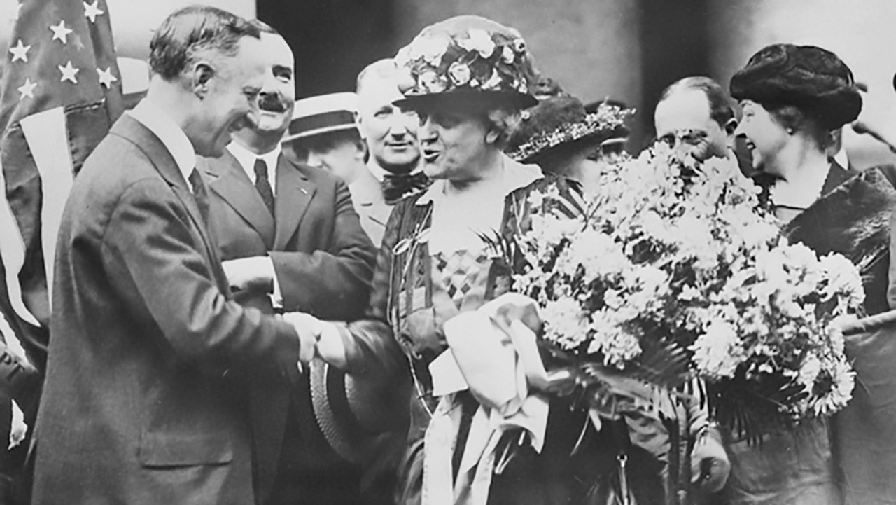 A group of suffragettes holding flower bouquets shaking the hands of dignitaries