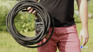 photo of the middle torso of a man and he is holding a garden hose coiled up in his right hand