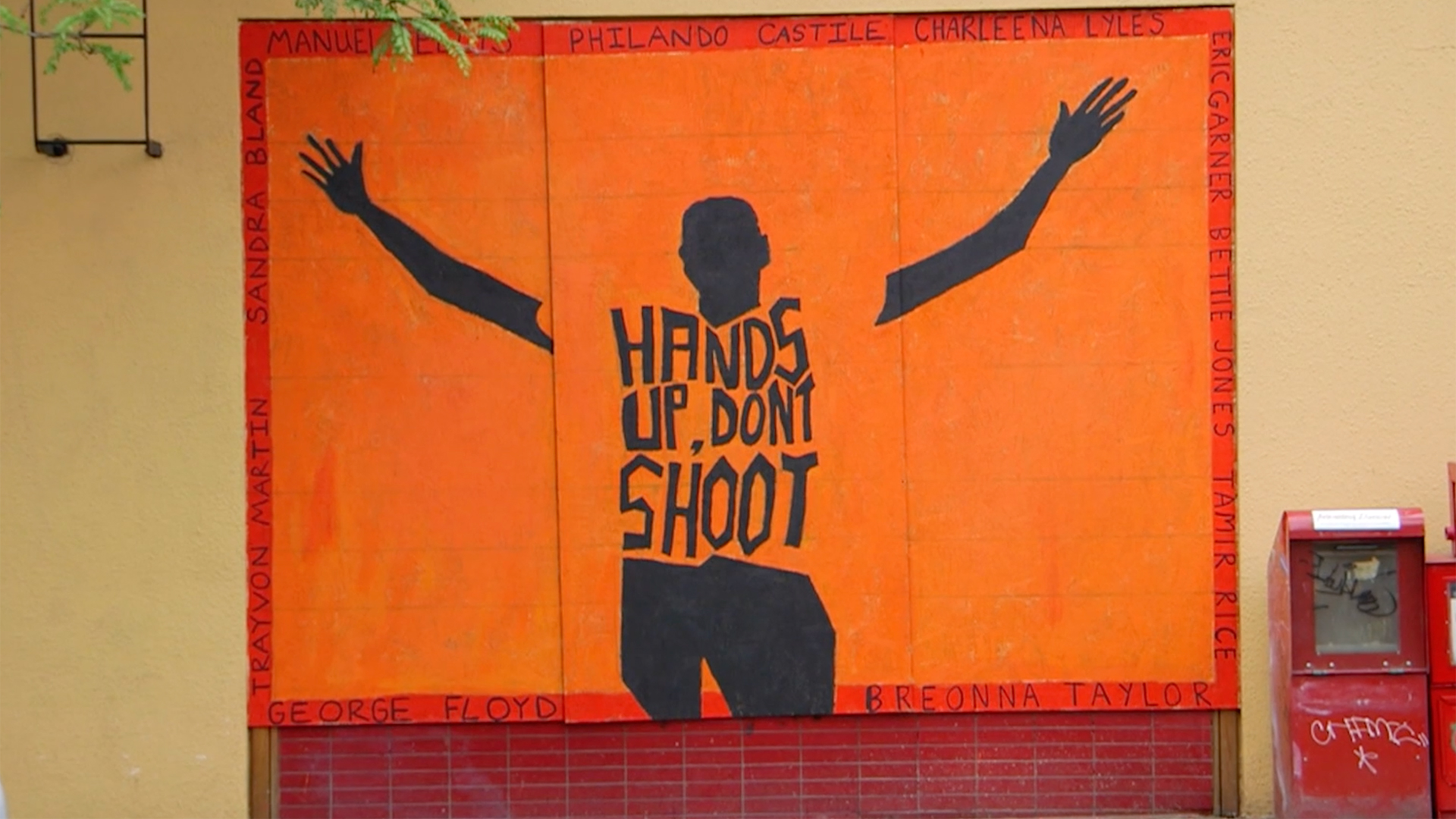 A mural depicting the silhouette of a Black man from behind with "Hands Up, Don't Shoot," written on his back