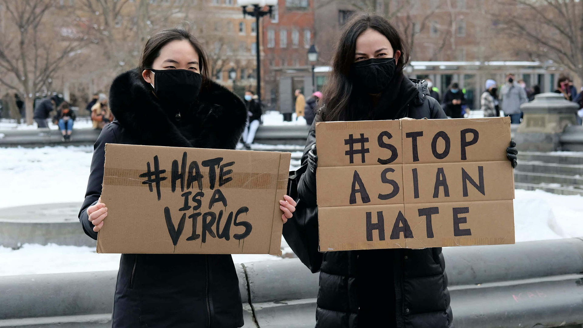 Two women stand by a fountain holding signs about stopping Asian hate
