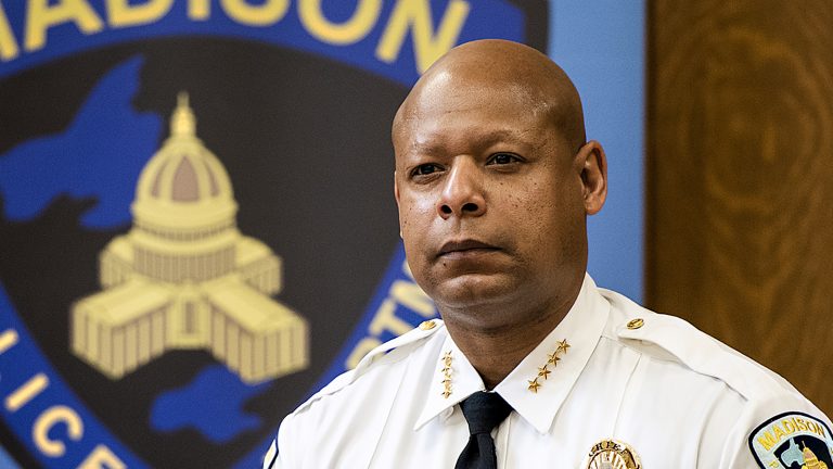Madison Police Chief Shon Barnes standing in front of Madison Police Department logo