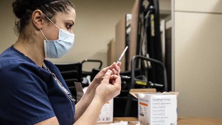 Nurse wearing mask holds a syringe with a COVID-19 vaccine