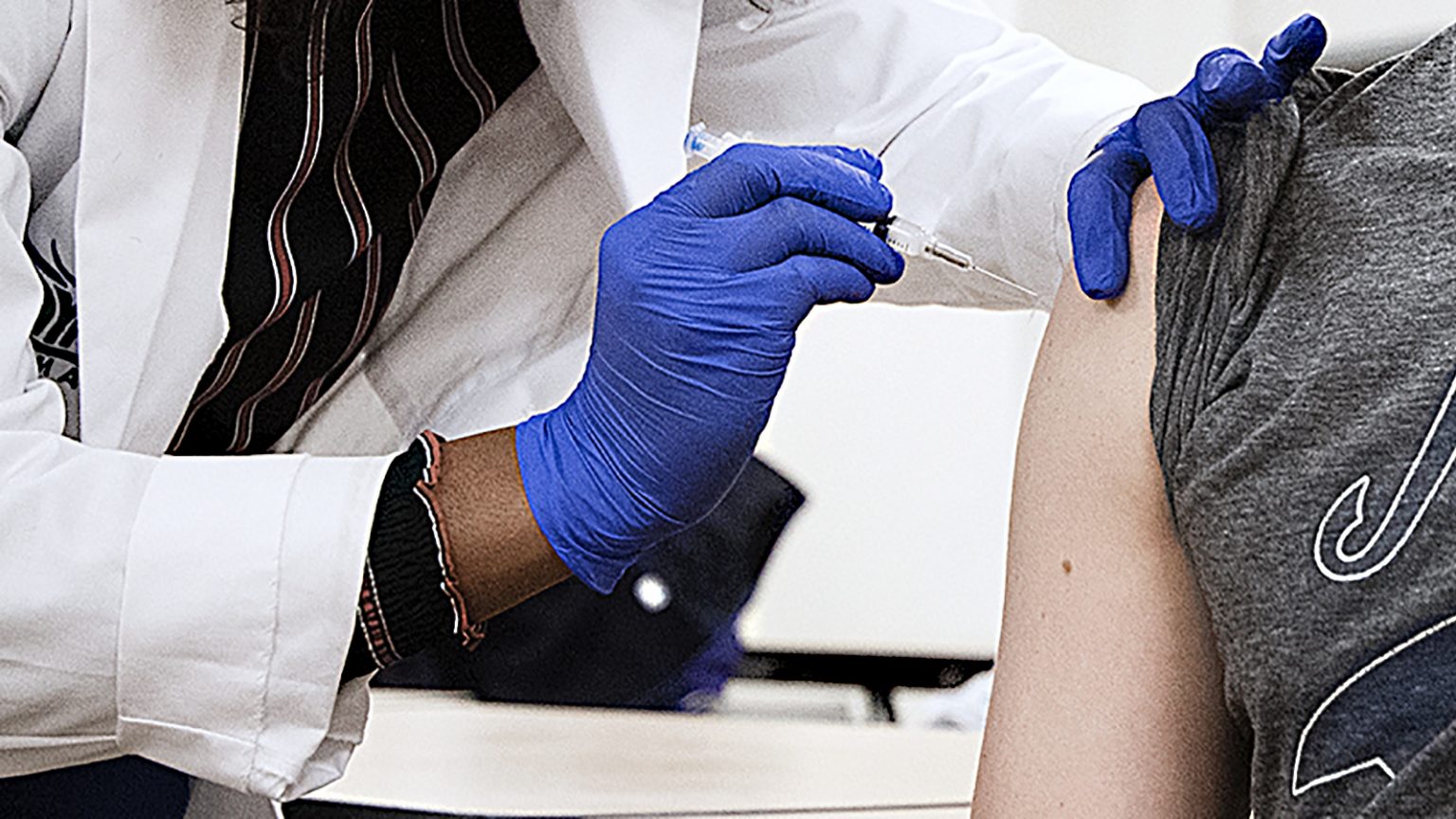 Gloved hands holding syringe inject a COVID-19 vaccine into an upper arm.