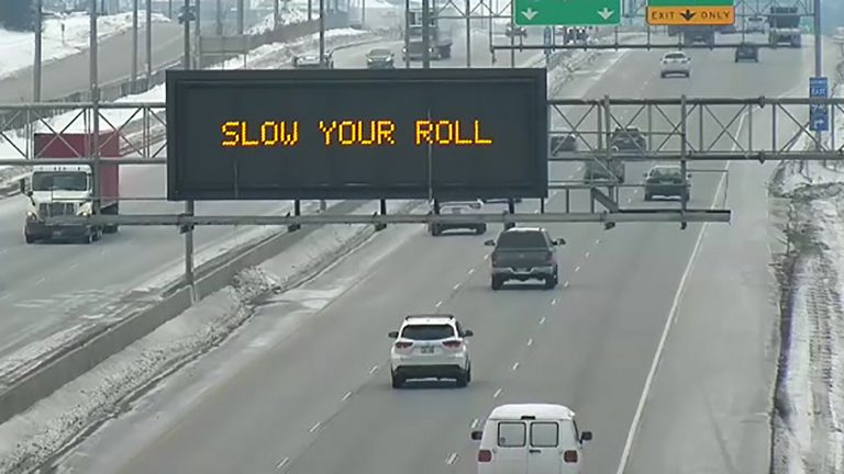 A digital traffic sign over a highway reads Slow Your Roll.