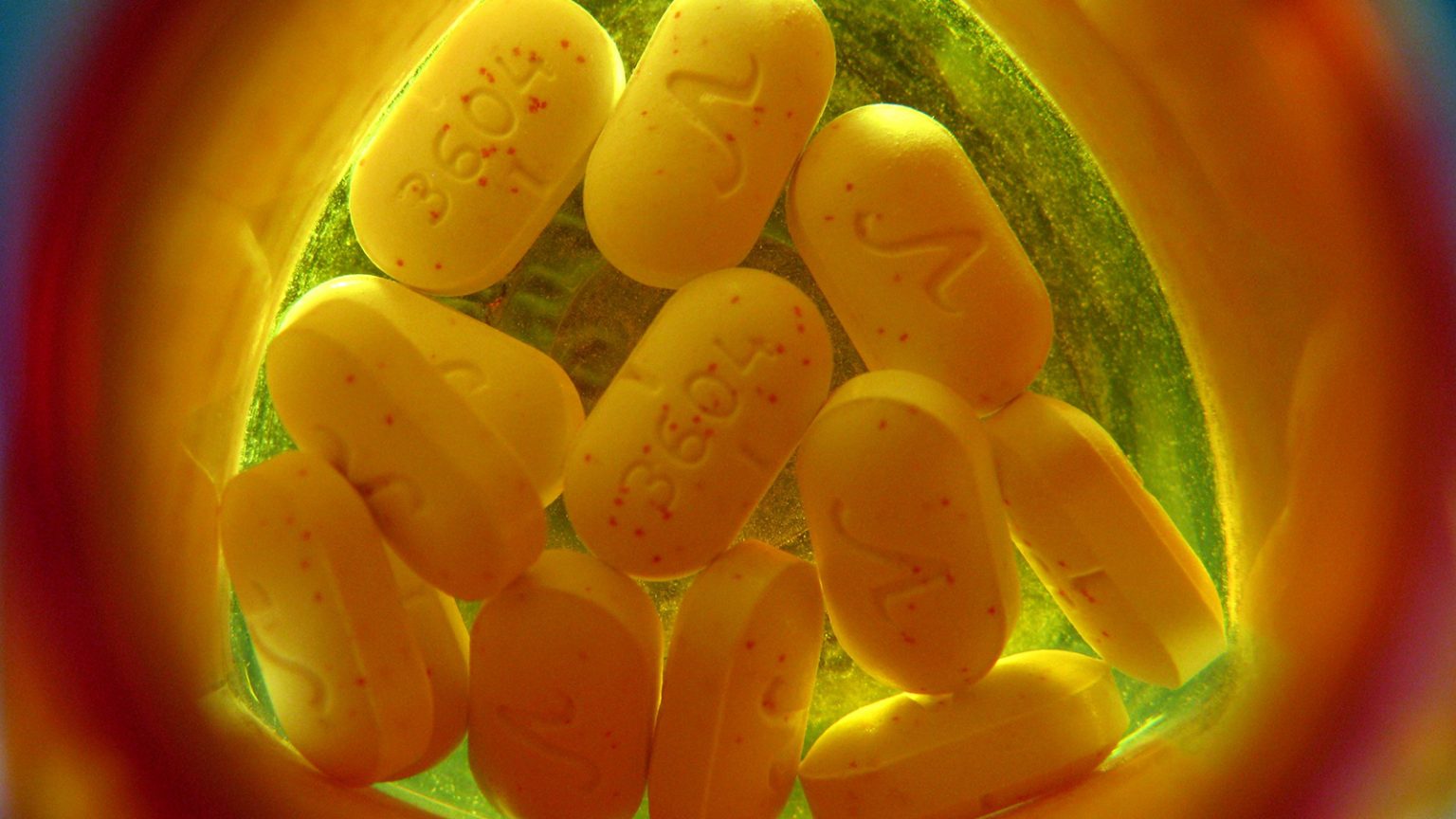 A dozen pills sit at the bottom of an orange prescription medication container.