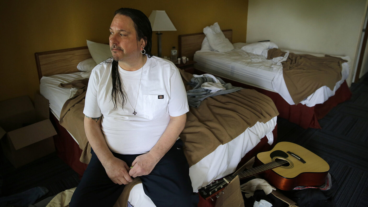 Christopher Kartsounes sitting on a bed in his room at an inn in Appleton, Wisconsin.