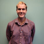 A young man stands in a red-purple button-down shirt