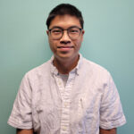 A young man stands in a white cotton button down shirt