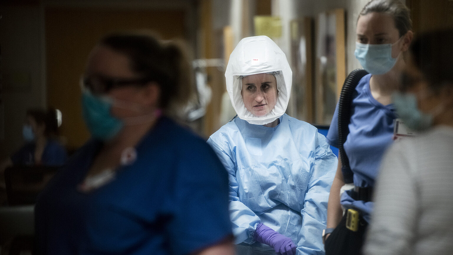 Nurses and doctors wearing personal protective equipment walk through a hallway.