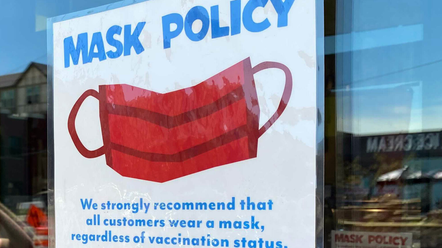 A sign on a door reads Mask Policy: We strongly recomment that all customers wear a mask, regardless of vacciation status.