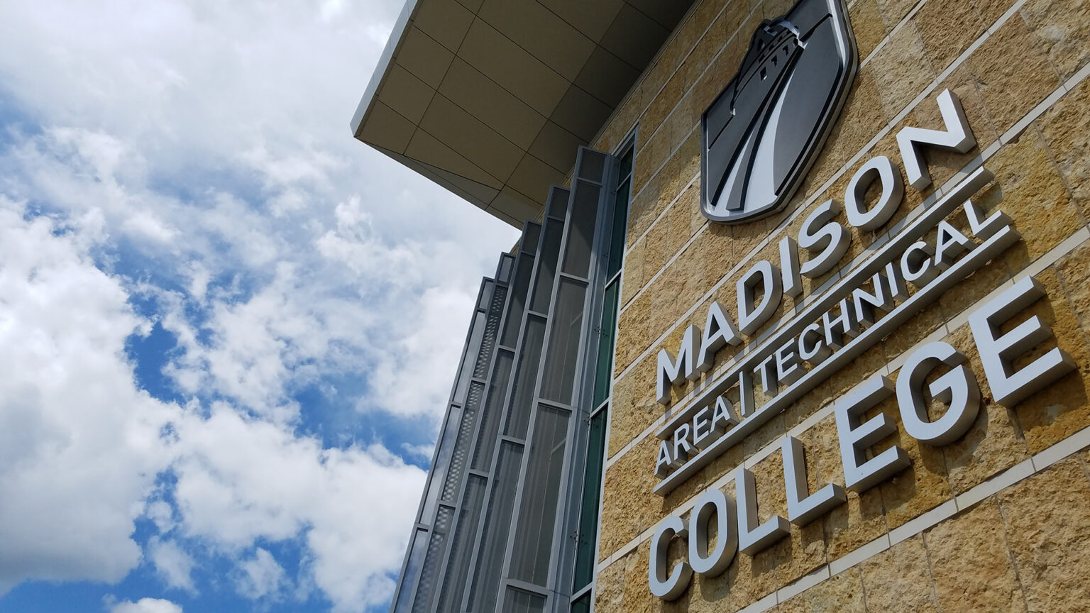 Madison Area Technical College sign on stone wall with blue sky and clouds in background