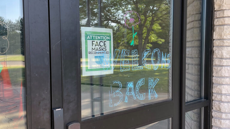 A door to the Tomahawk schools complex with a sign stating Attention Face Masks Recommended and a painted Welcome Back message.