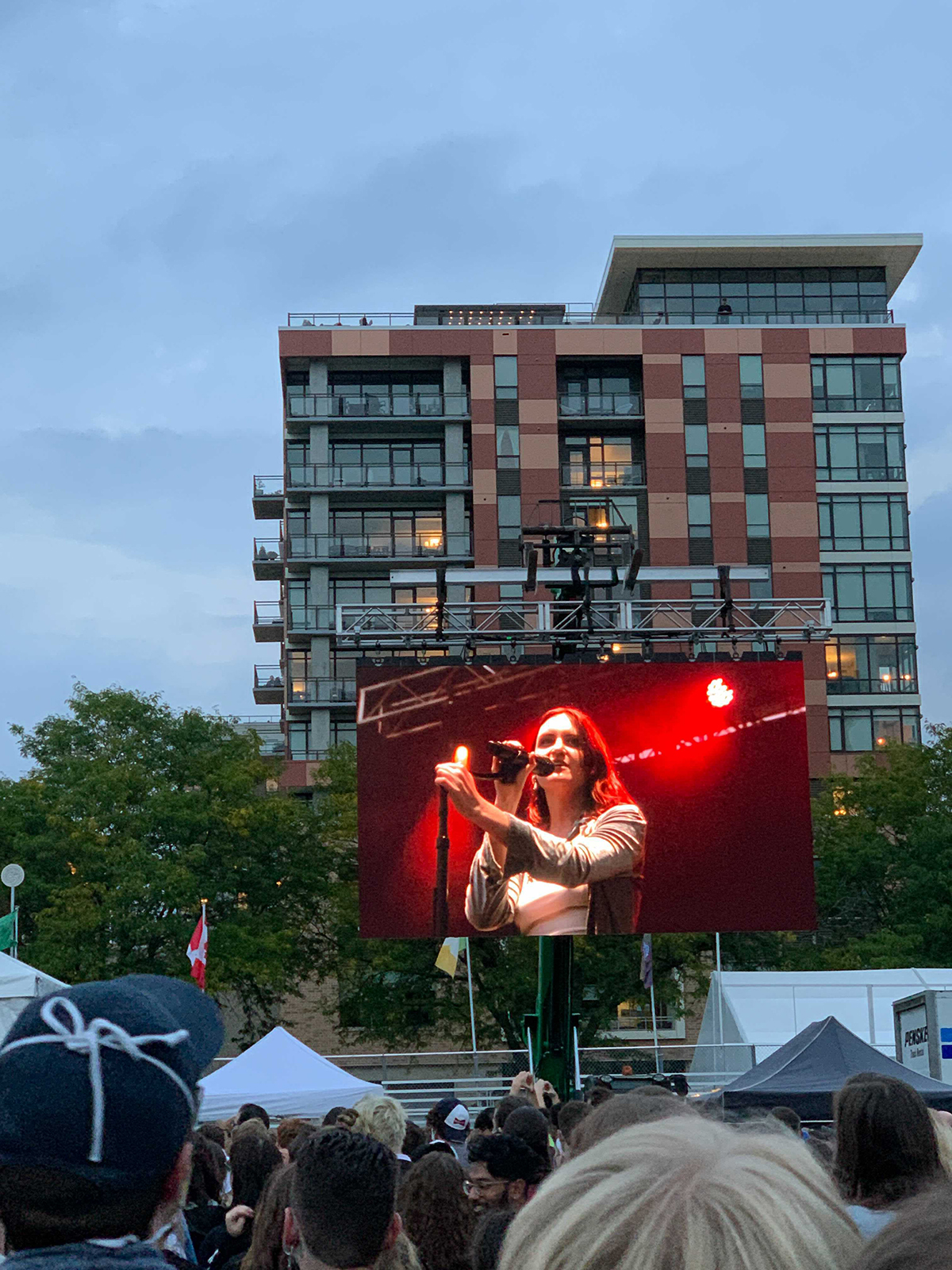 A large electronic screen shows the lead singer of the pop band MUNA playing before an outdoor crowd at Breese Stevens Field in Madison, Wisconsin.