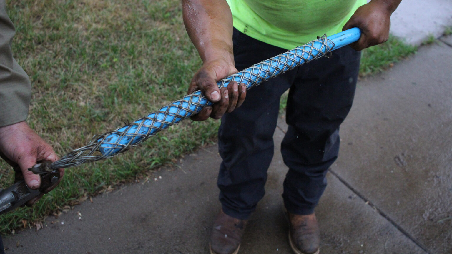 Workers hold a blue replacement water pipe surrounded by metal netting.