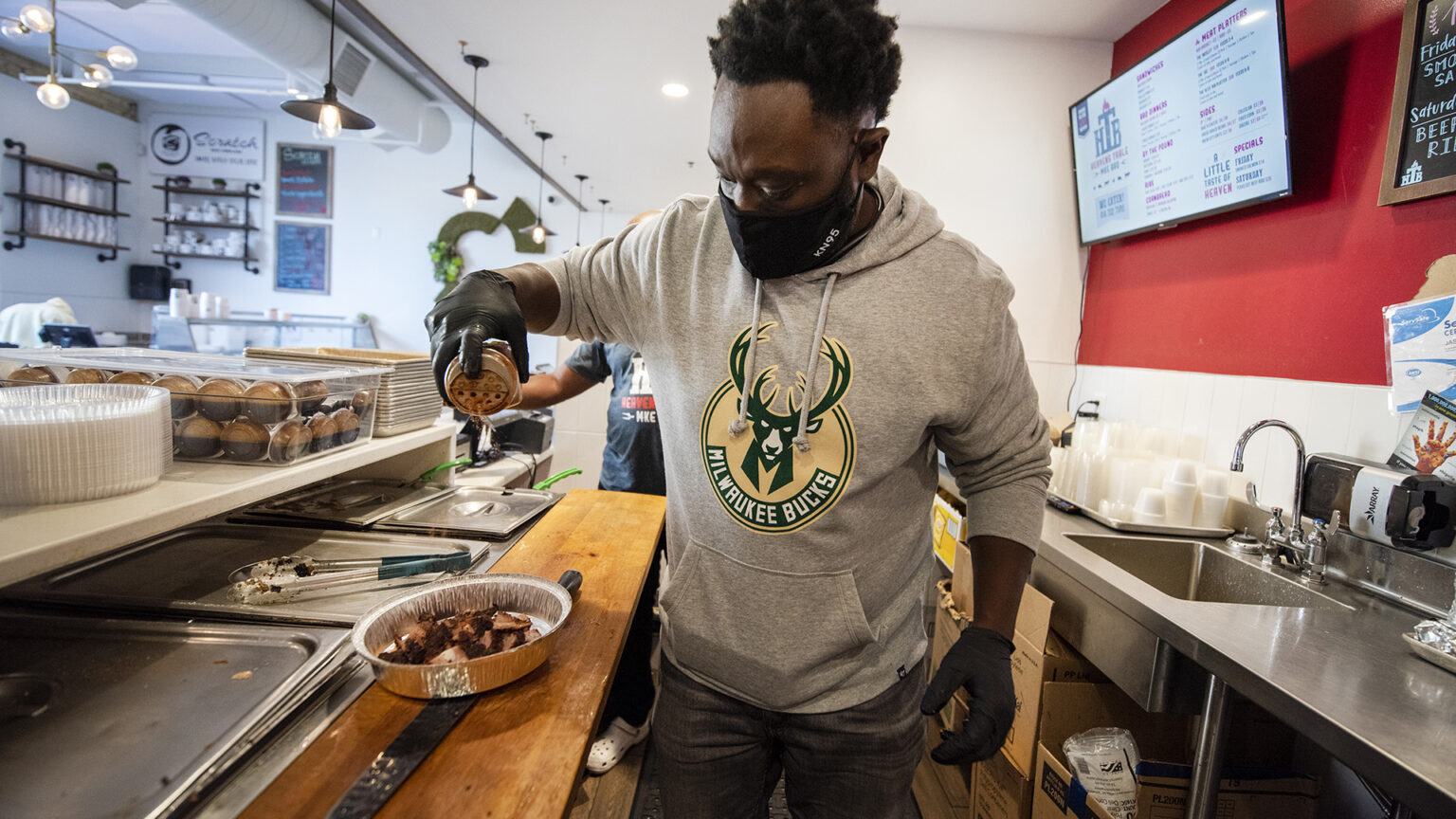 Jason Alston sprinkles seasoning on meat in a to-go container behind a counter.