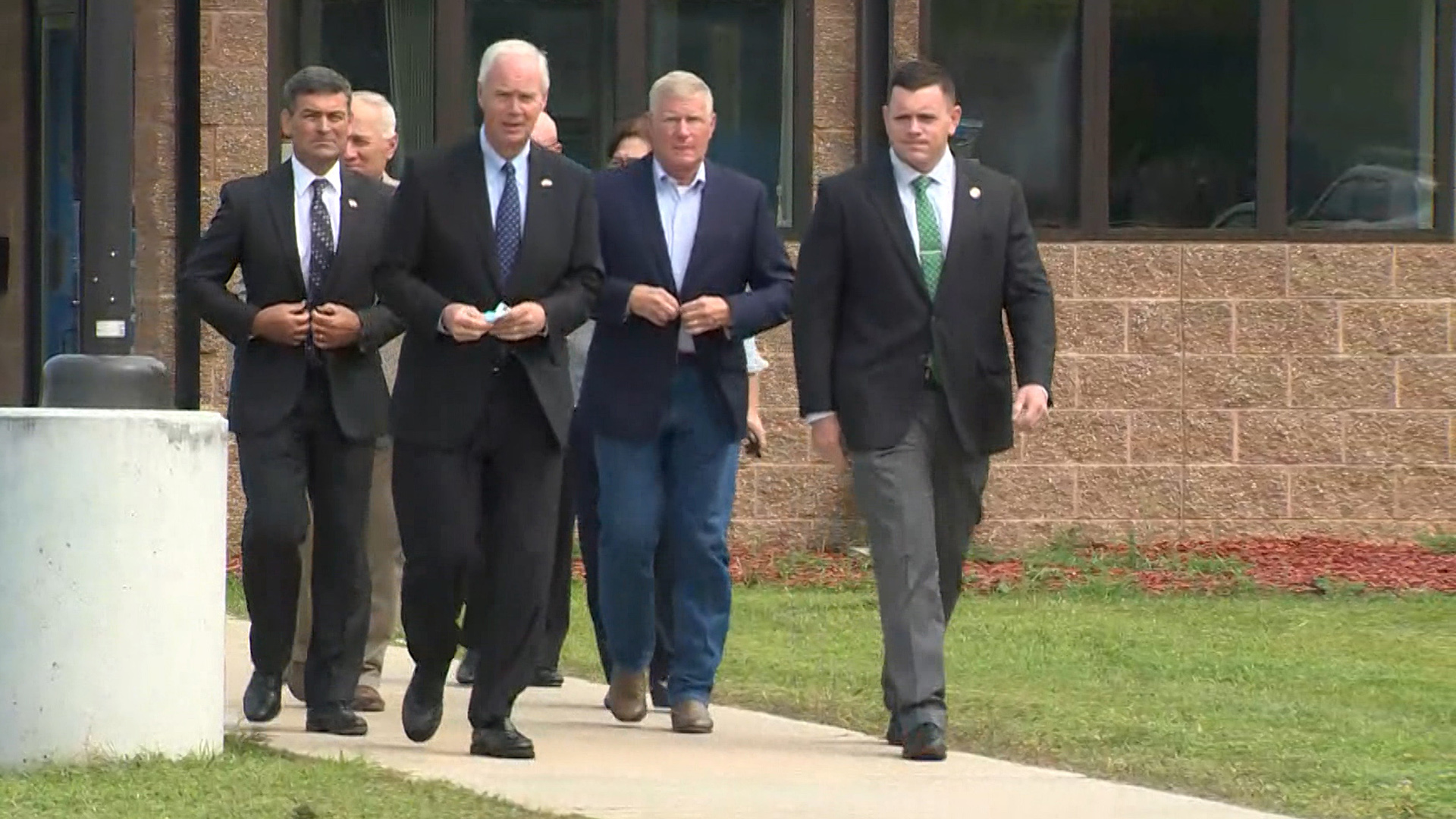 Ron Johnson and other law makers walk down a sidewalk from the entrance of a building.