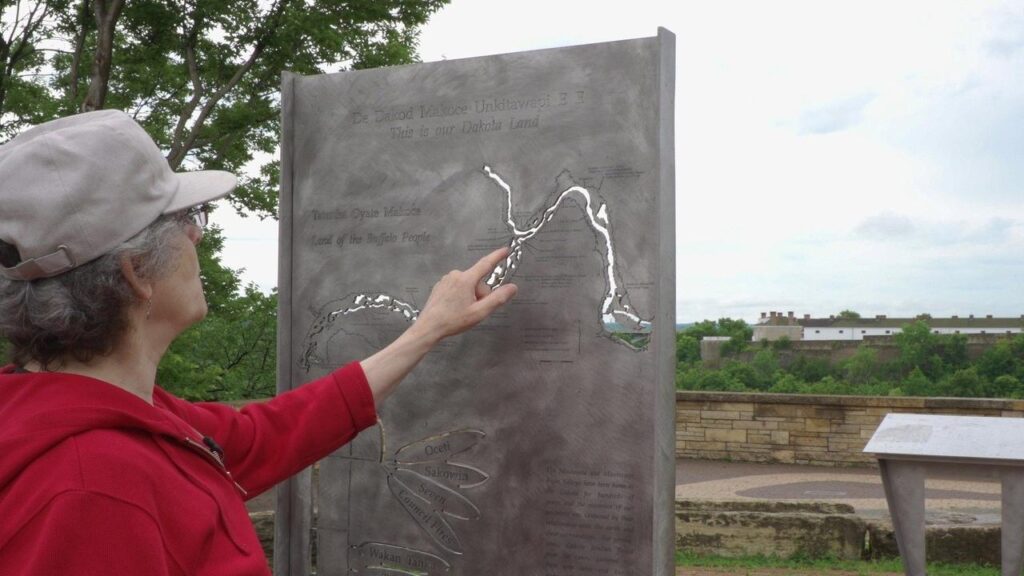 A woman examines an outdoor map called "This is our Dakota Land"