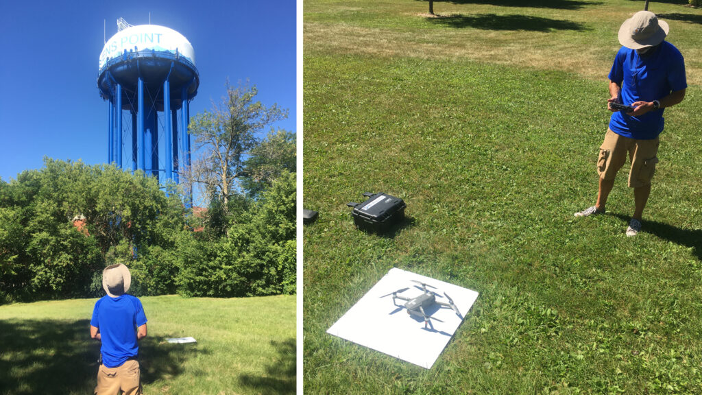 A camera man flying a drone by a water tower and landing it on a white board