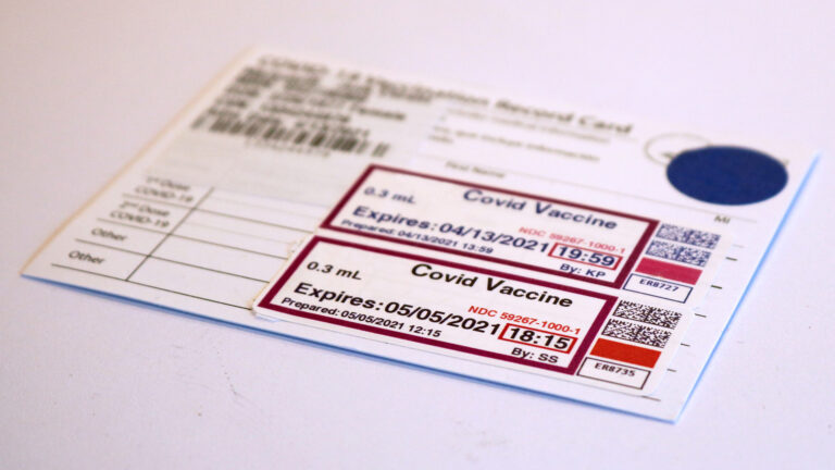 A COVID-19 vaccination record card with stickers noting two doses sits on a white surface.