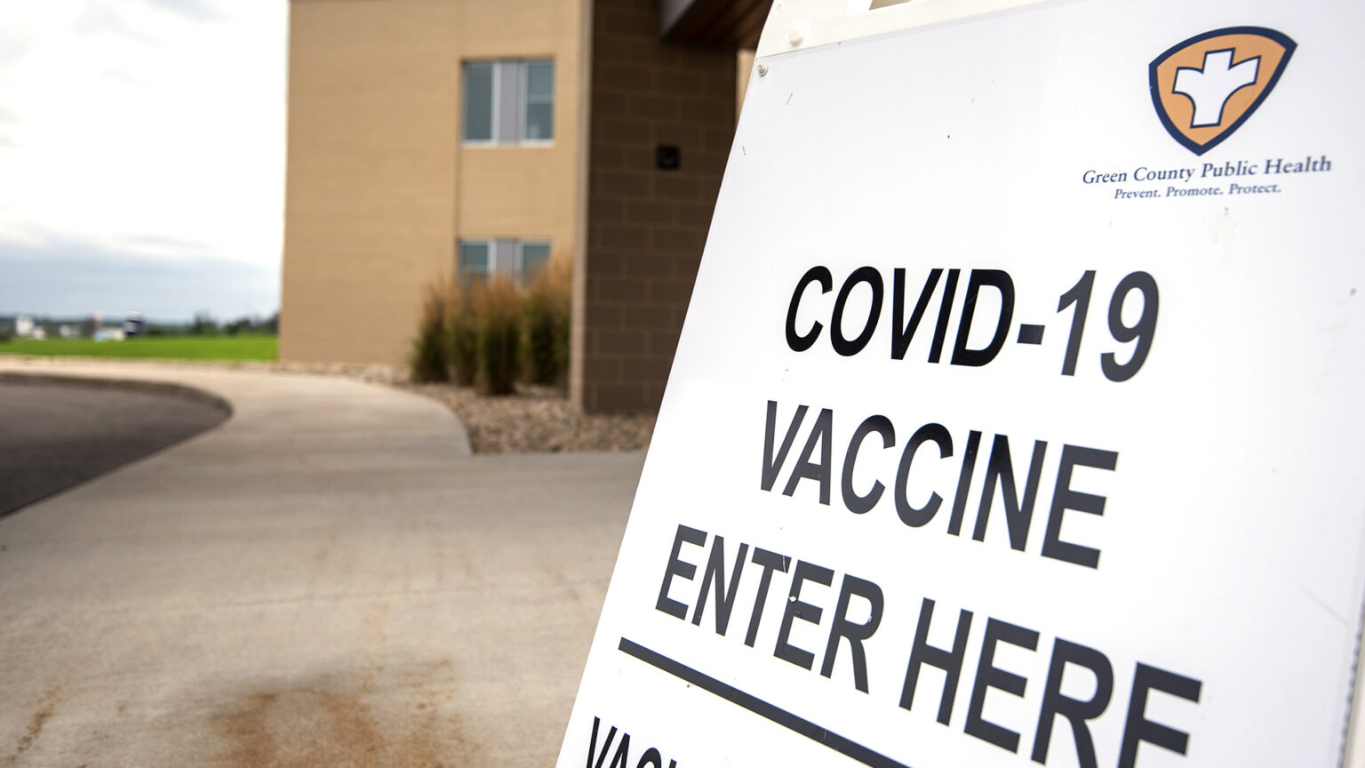 A sidewalk sign reading COVID-19 Vaccine Enter Here stands in front of a building entrance.