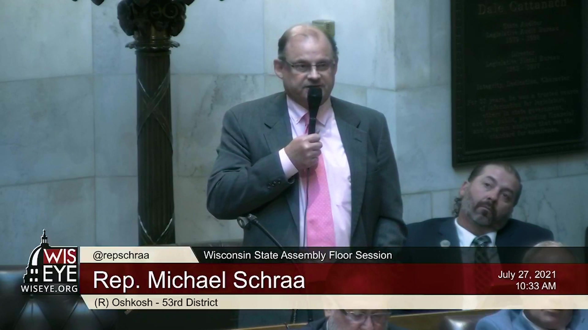 Michael Schraa holds a microphone and speaks in the Wisconsin Assembly chambers.