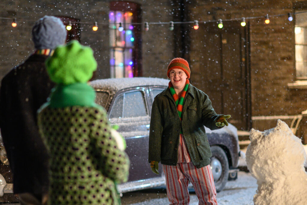 A young man standing in the snow smiles at his friends.