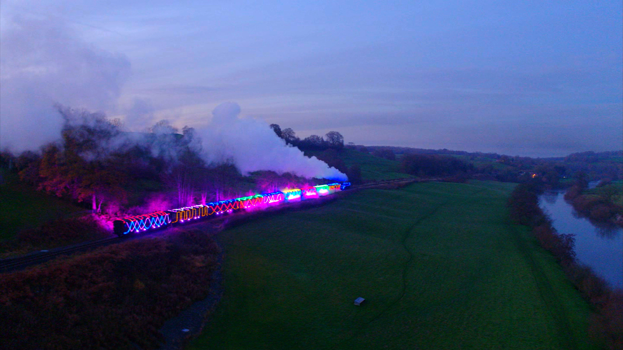 An antique train decorated with colorful Christmas lights rides the rails of the countryside.