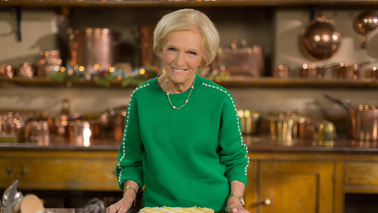 Chef and baker Mary Berry stands in a kitchen and smiles at the camera.