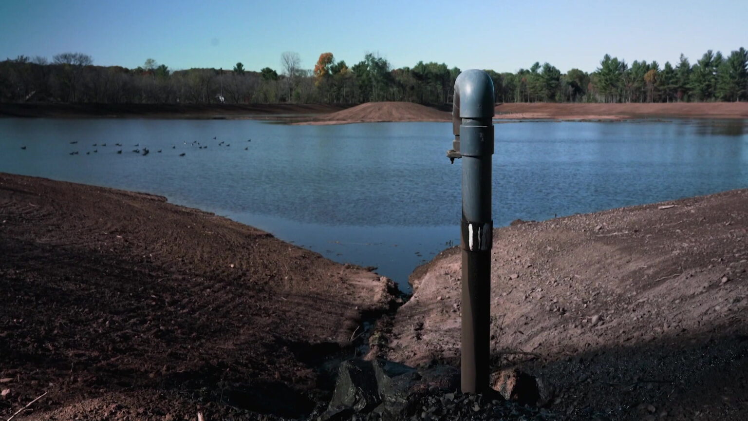 A pond is surrounded by earthen berms with trees in the background.