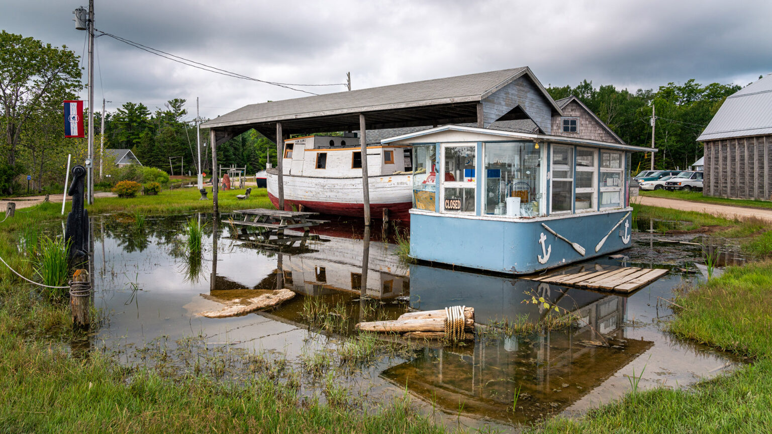 Flood waters surround a pier area with a small vendor building and wooden boat under a covered shelter.