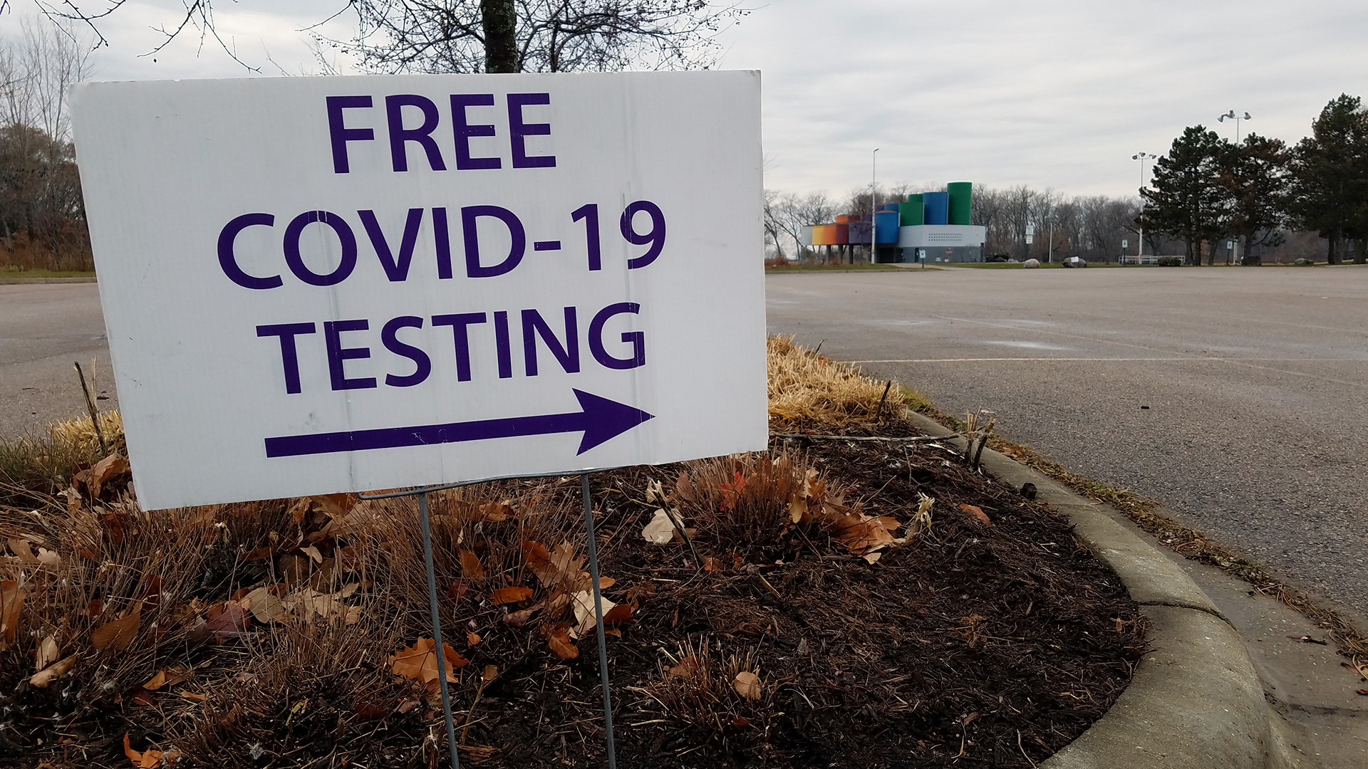 A lawn sign in a parking lot divider reads "FREE COVID-19 TESTING" with an arrow pointing right.