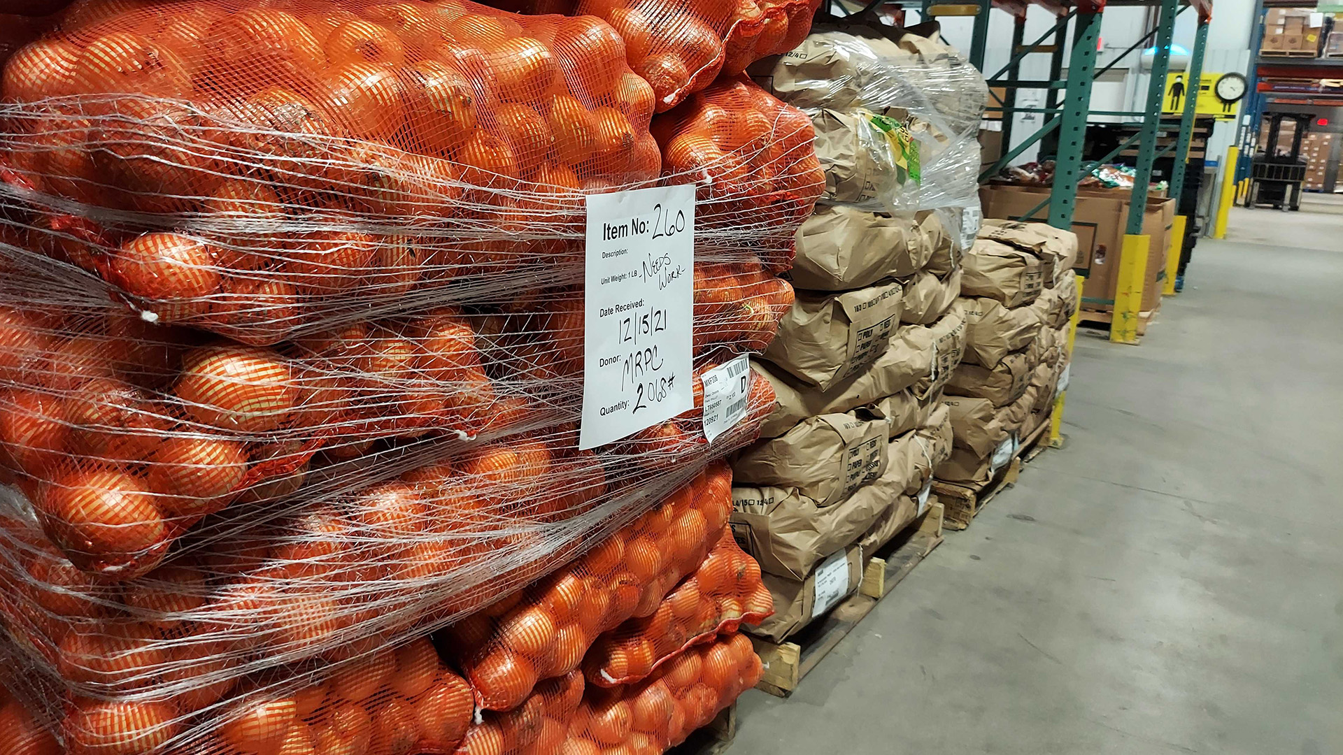 Bags of onions are stacked on a pallet alongside other bulk packaged food inside a warehouse.