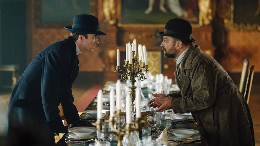 Two men lean towards each other in discussion over a table set for dinner.