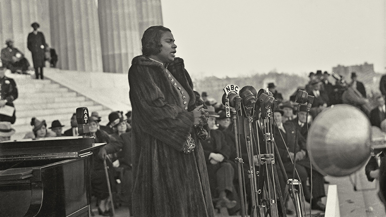 A female opera singer sings at a microphone in front of a large crowd.