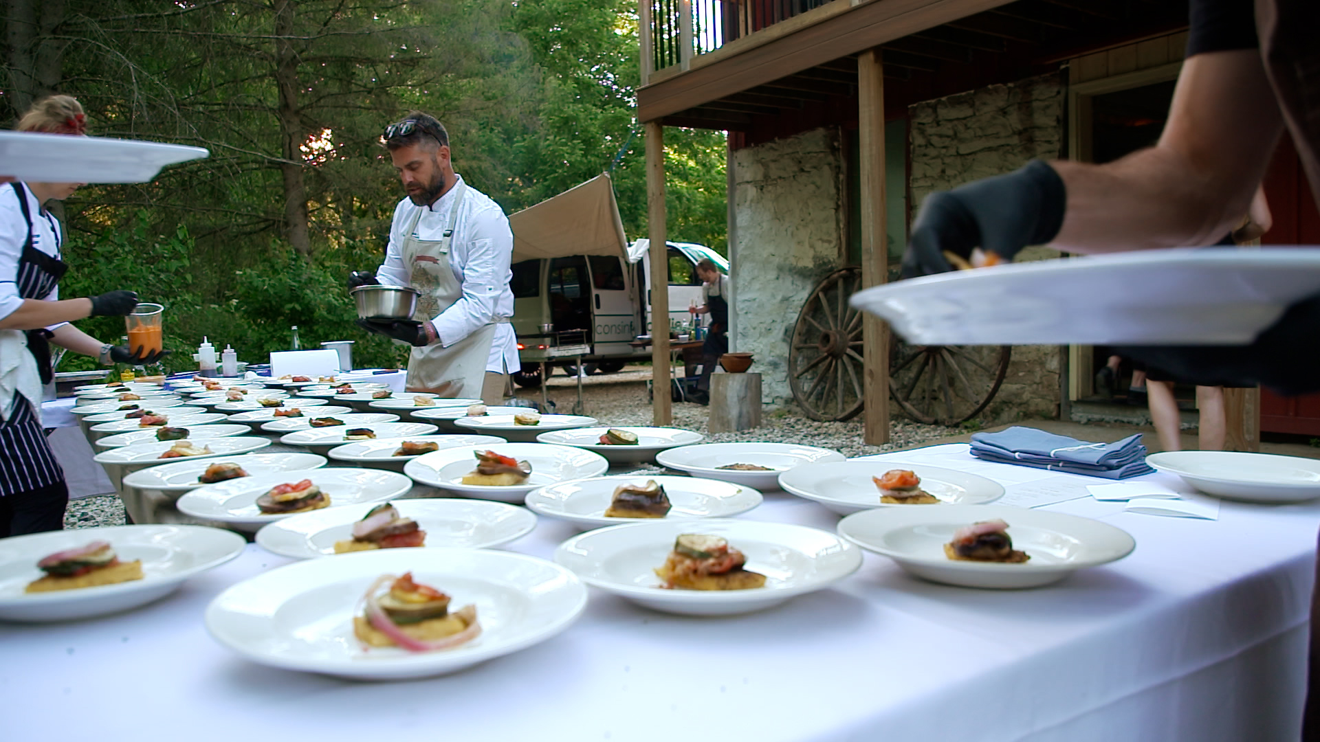 A chef adds food to white plates on a large table.