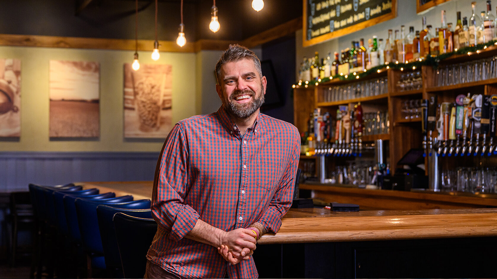 Wisconsin Foodie host Luke Zahm leans against a bar in a red plaid shirt, smiling