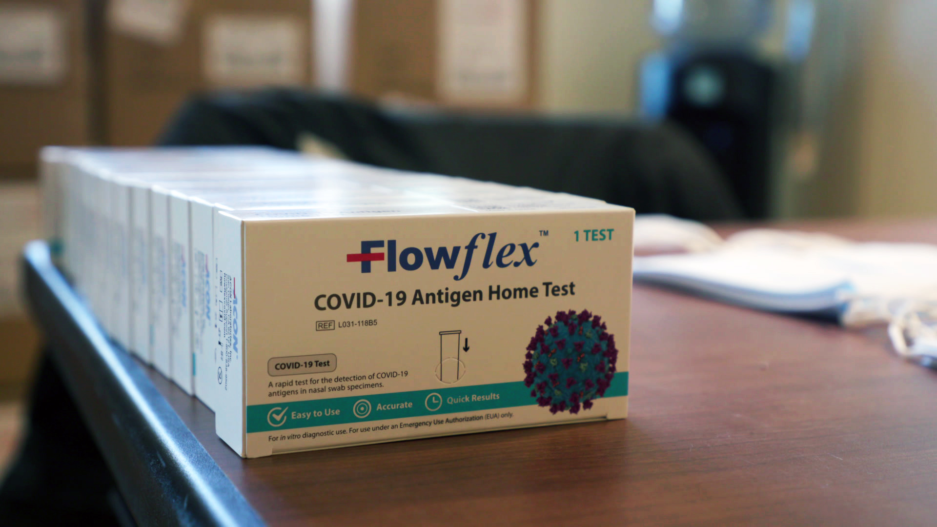 A row of FlowFlex COVID-19 Antigen Home Test boxes sits on top of a table.