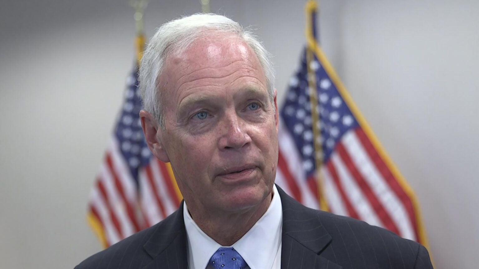 Ron Johnson speaks in a room with flags in the background.