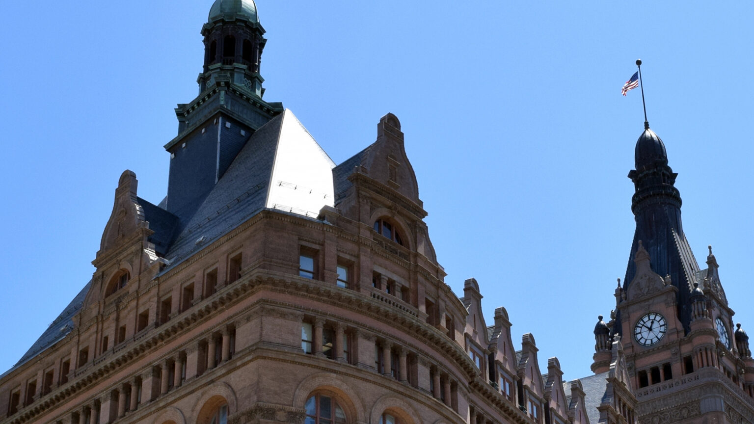 The top floors and spires of Milwaukee City Hall contrast with a cloudless, blue sky.