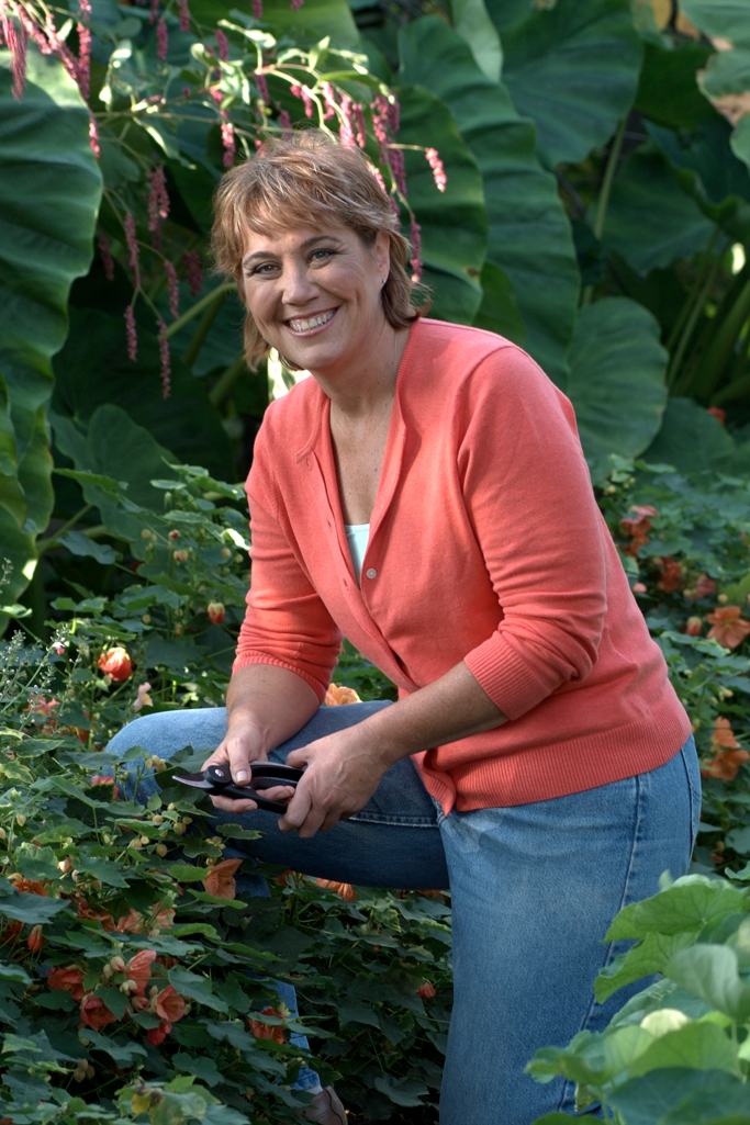 Melinda Myers kneeling by some flowering shrubs along a path in a garden