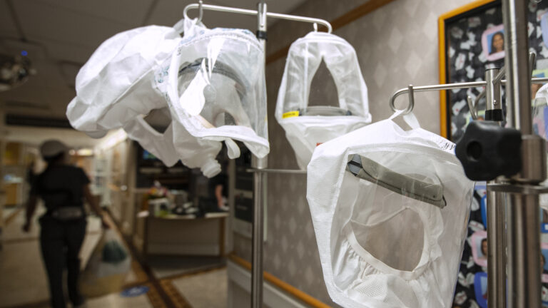Multiple PAPR hoods hang on medical IV poles in a hospital hallway.