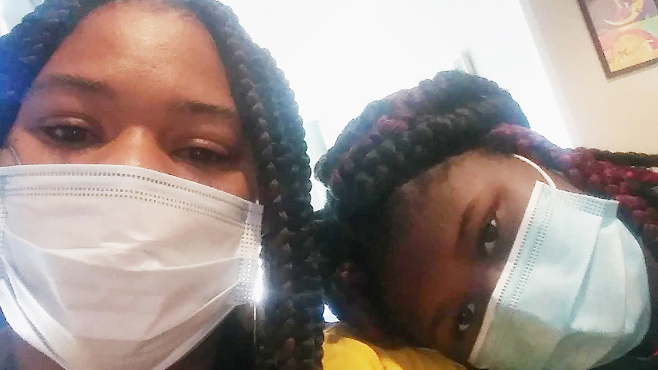 A mother and daughter pose for a portrait while wearing medical face masks.
