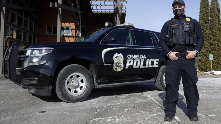 Nate Ness stands next to a police SUV with its side doors  featuring a badge graphic and the words Oneida Police.