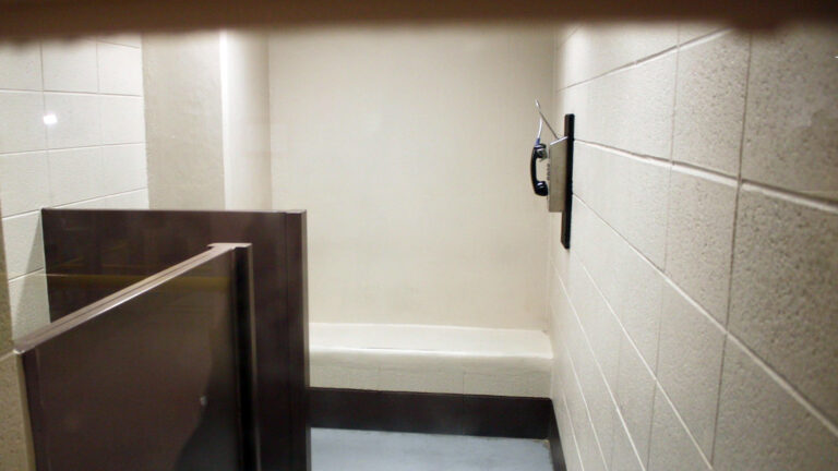 A phone is mounted on a cinder-block wall inside a room in a jail.