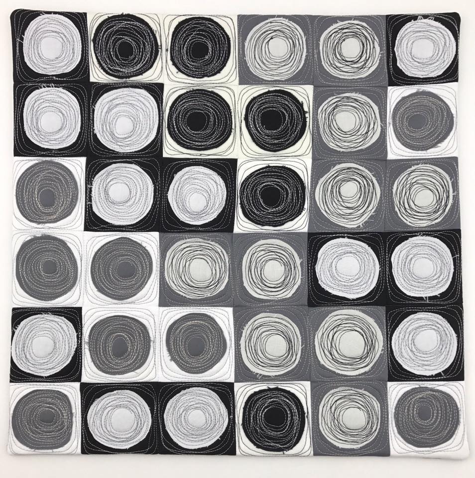 A quilt made of a checkerboard of grey, concentric circles.
