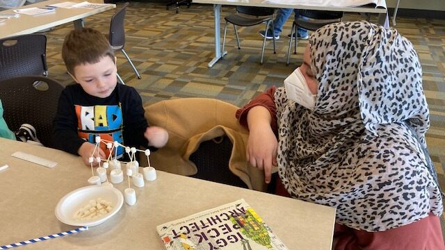 woman and child at table putting toothpicks and marshmellows together creating a structure