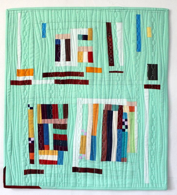 A seafoam green quilt with strips of multicolor fabric crossing in a random pattern