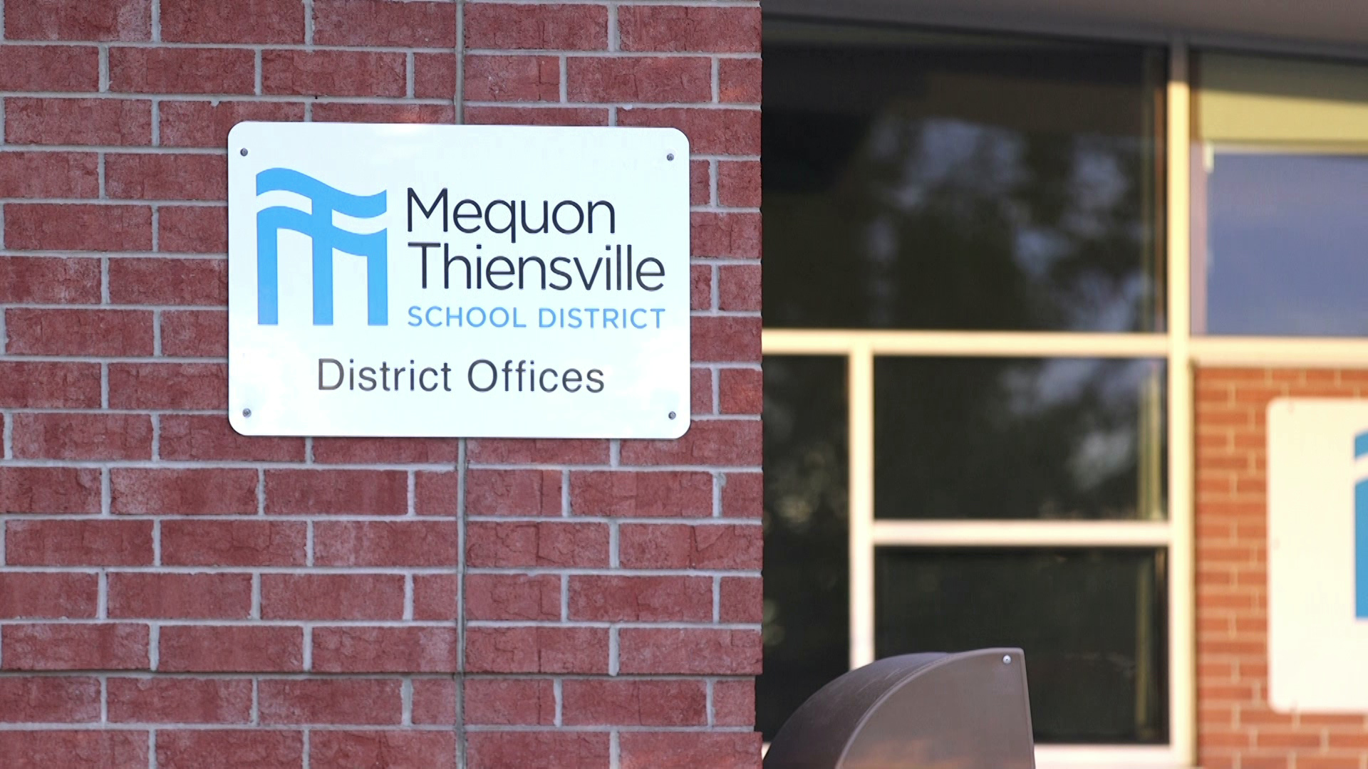 A sign on a brick wall reads "Mequon Thiensville School District - District Offices"